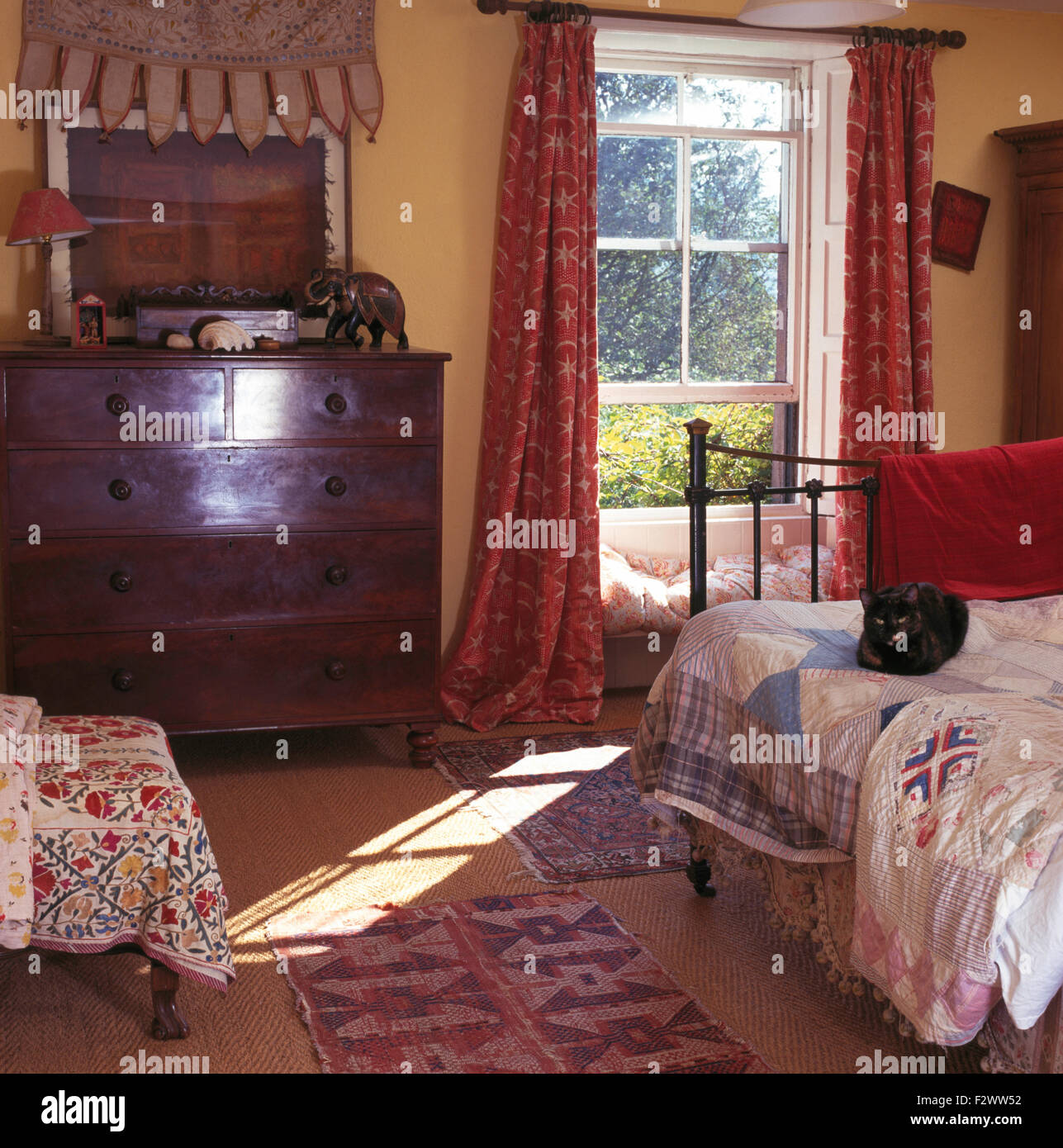 Cassettiera antica accanto alla finestra con tende rosse nella camera da letto degli anni novanta Foto Stock