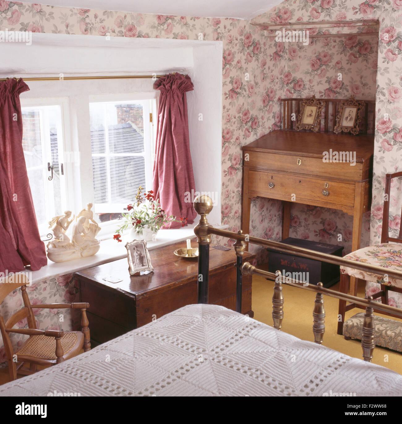 Rose carta da parati con motivi geometrici e rosa tende in novanta cottage camera da letto con un'antica scrivania in un angolo Foto Stock
