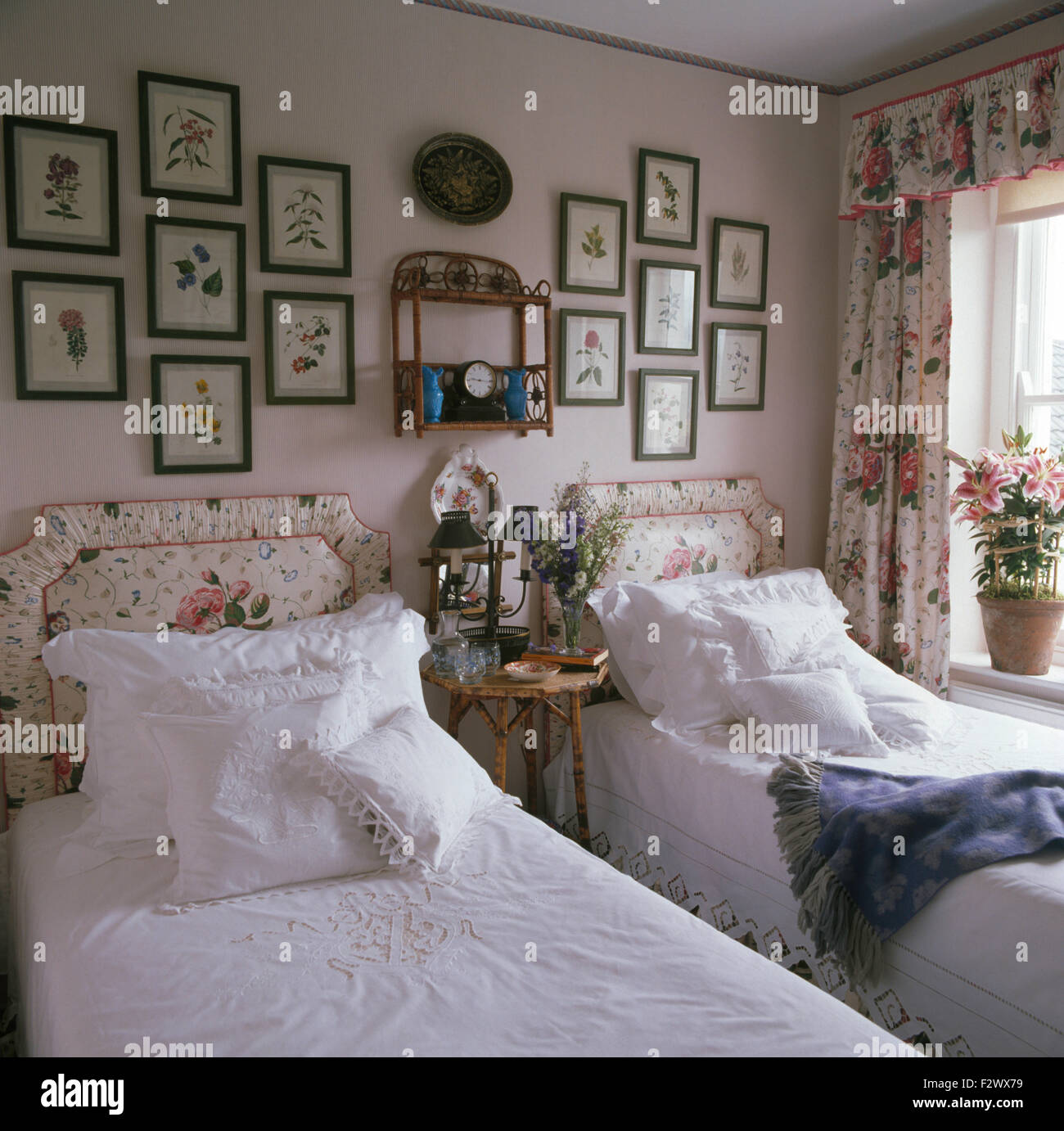 Incorniciato dalle stampe floreali sulla parete al di sopra di letti singoli con biancheria bianca e rosa imbottite testiere modellato Foto Stock