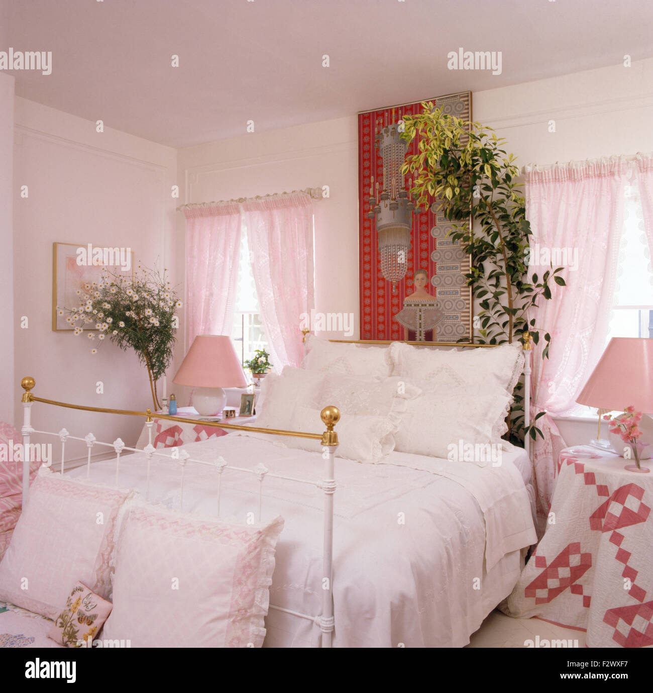 Pizzo Bianco rifilando i cuscini e il coperchio sul letto di ottone in camera da letto degli anni novanta con il rosa voile drappeggi su windows Foto Stock