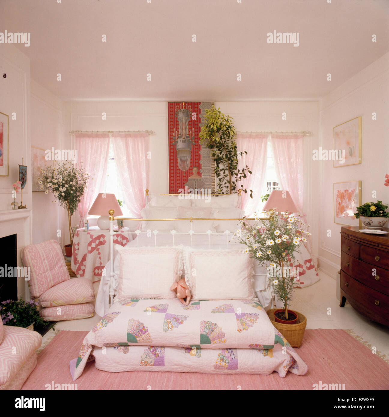 Patchwork cuscini sotto ottone bianco letto matrimoniale in camera da letto degli anni novanta con drappeggi rosa su windows Foto Stock