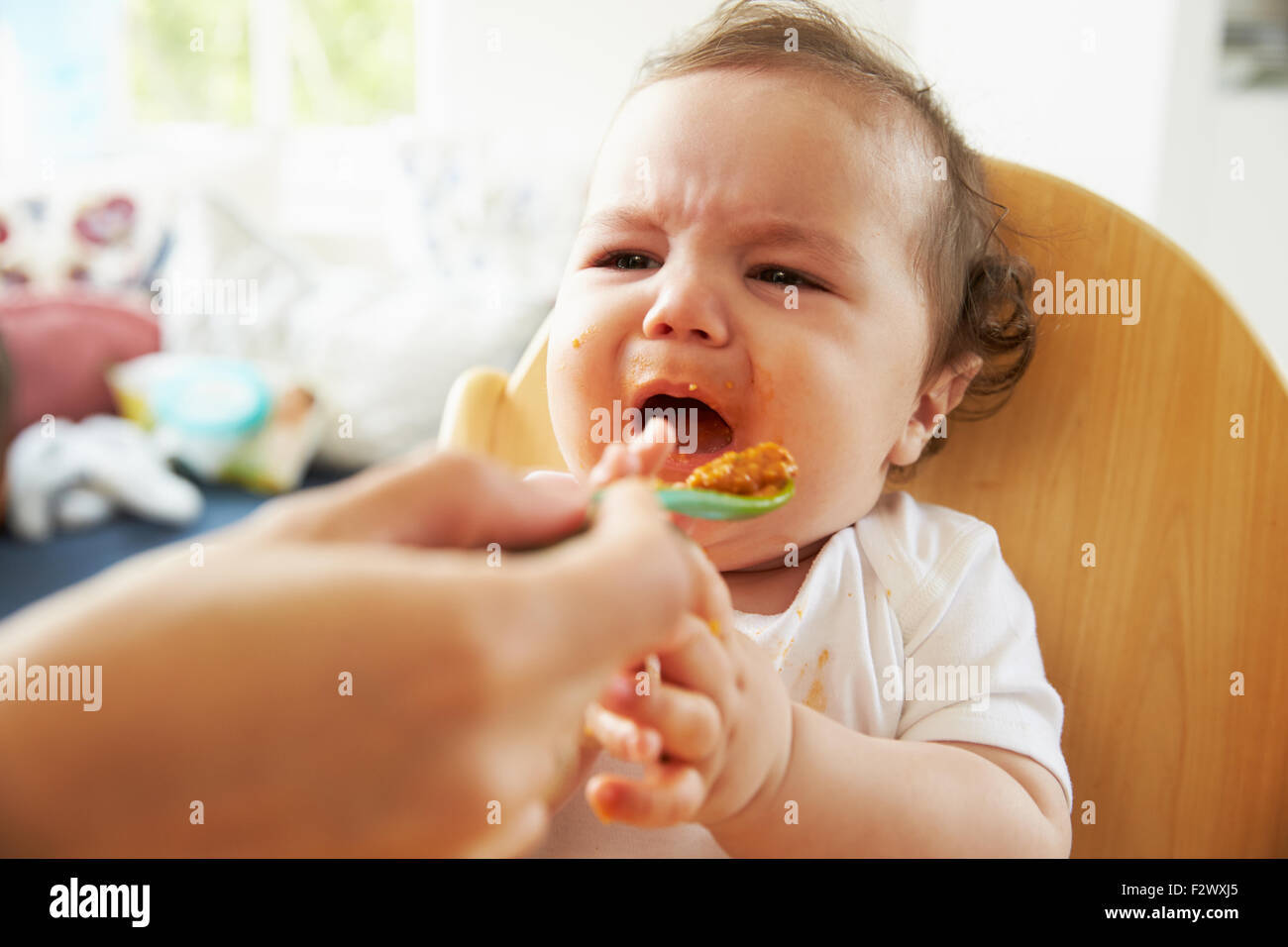 Infelice Baby essendo alimentato in alta sedia al momento dei pasti Foto Stock