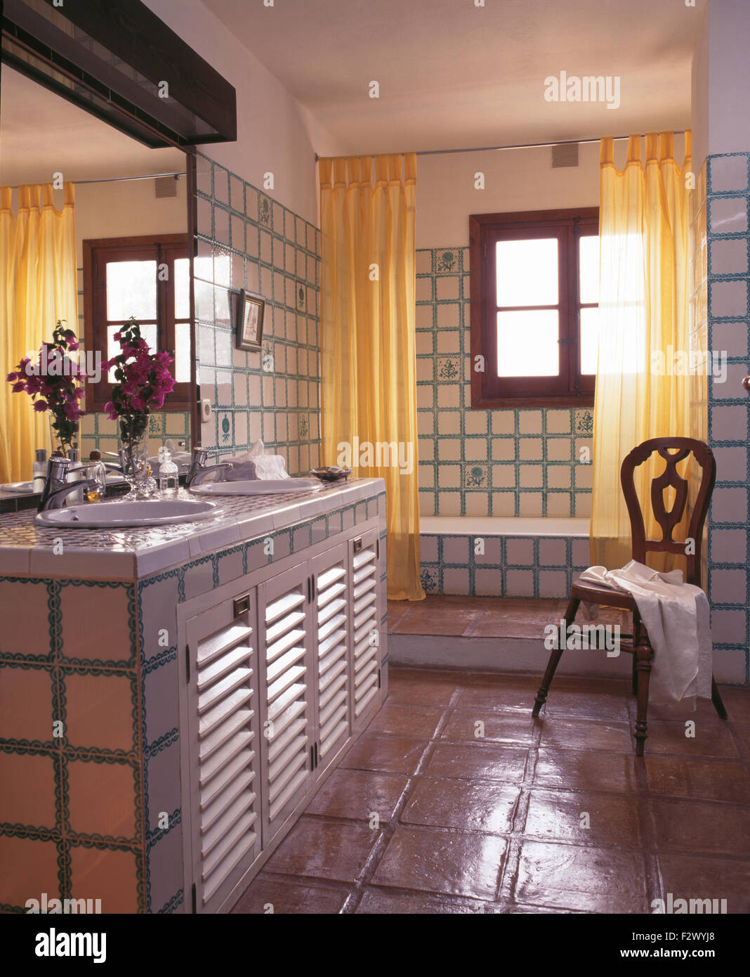 Il giallo tende da doccia su vasca da bagno in piastrelle paese spagnolo bagno con pavimento in piastrelle di terracotta Foto Stock
