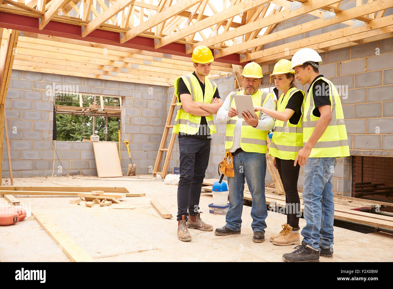 Builder sul sito alla ricerca a tavoletta digitale con apprendisti Foto Stock