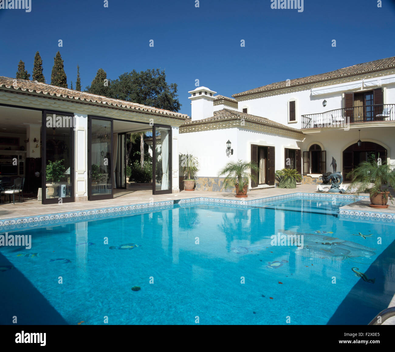 Il turchese piscina frontale di grande villa spagnola con porte in vetro scorrevoli su sala biliardo Foto Stock