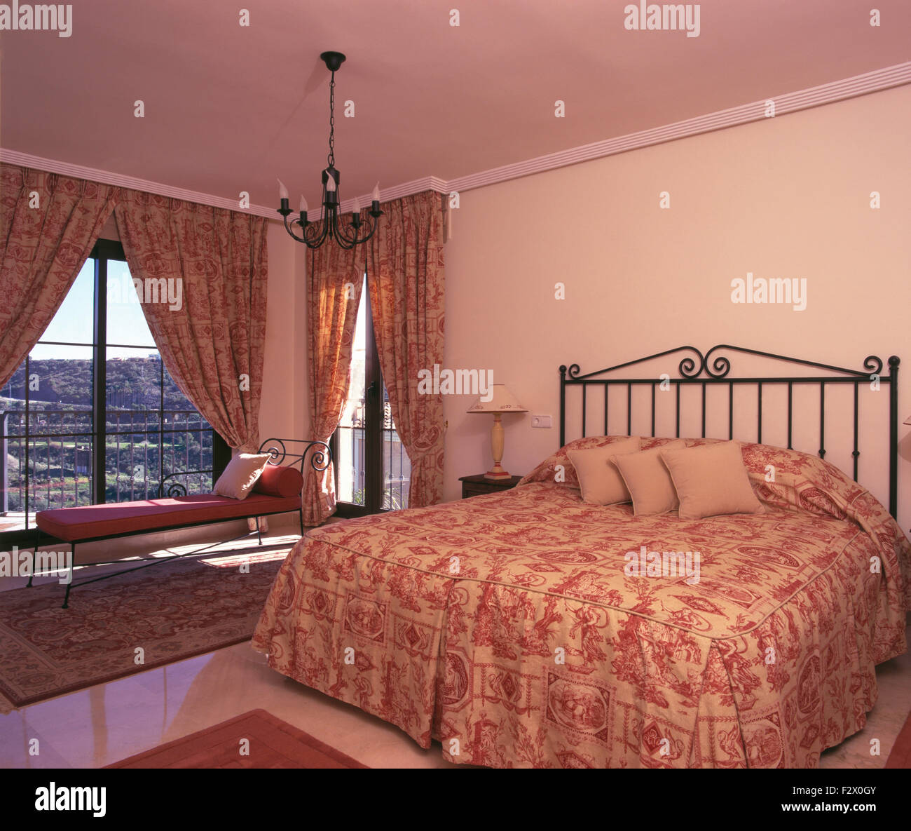 Rosa quilt modellato sul letto di metallo in spagnolo camera da letto con il coordinamento di tende su porte di vetro per balcone Foto Stock