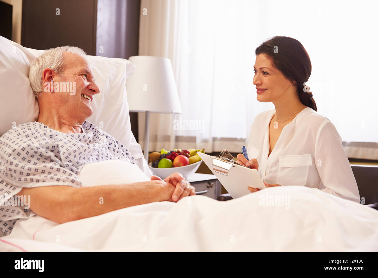 Medico donna parlando a Senior paziente di sesso maschile nel letto di ospedale Foto Stock