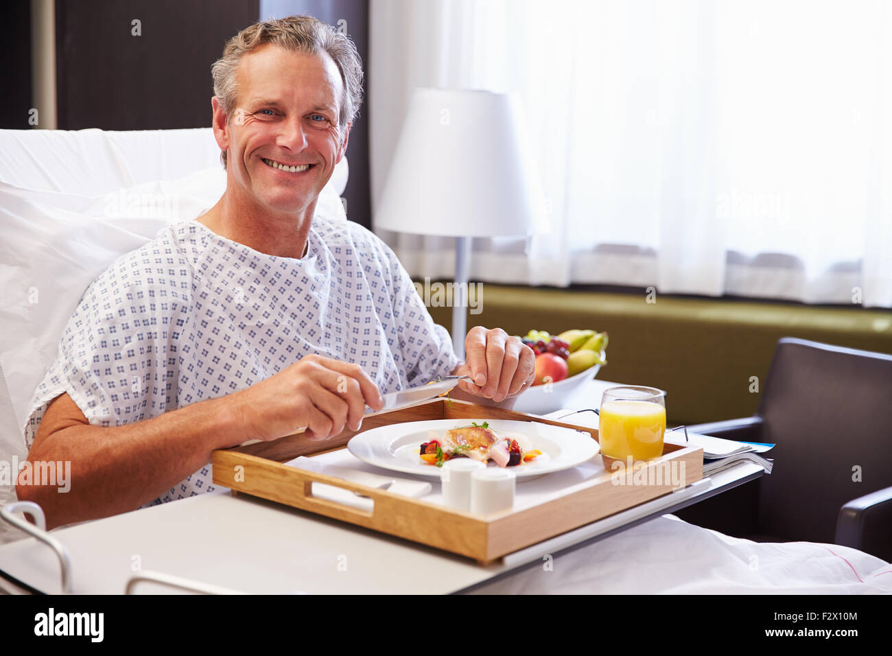 Paziente di sesso maschile nel letto di ospedale mangiare pasto dal vassoio Foto Stock