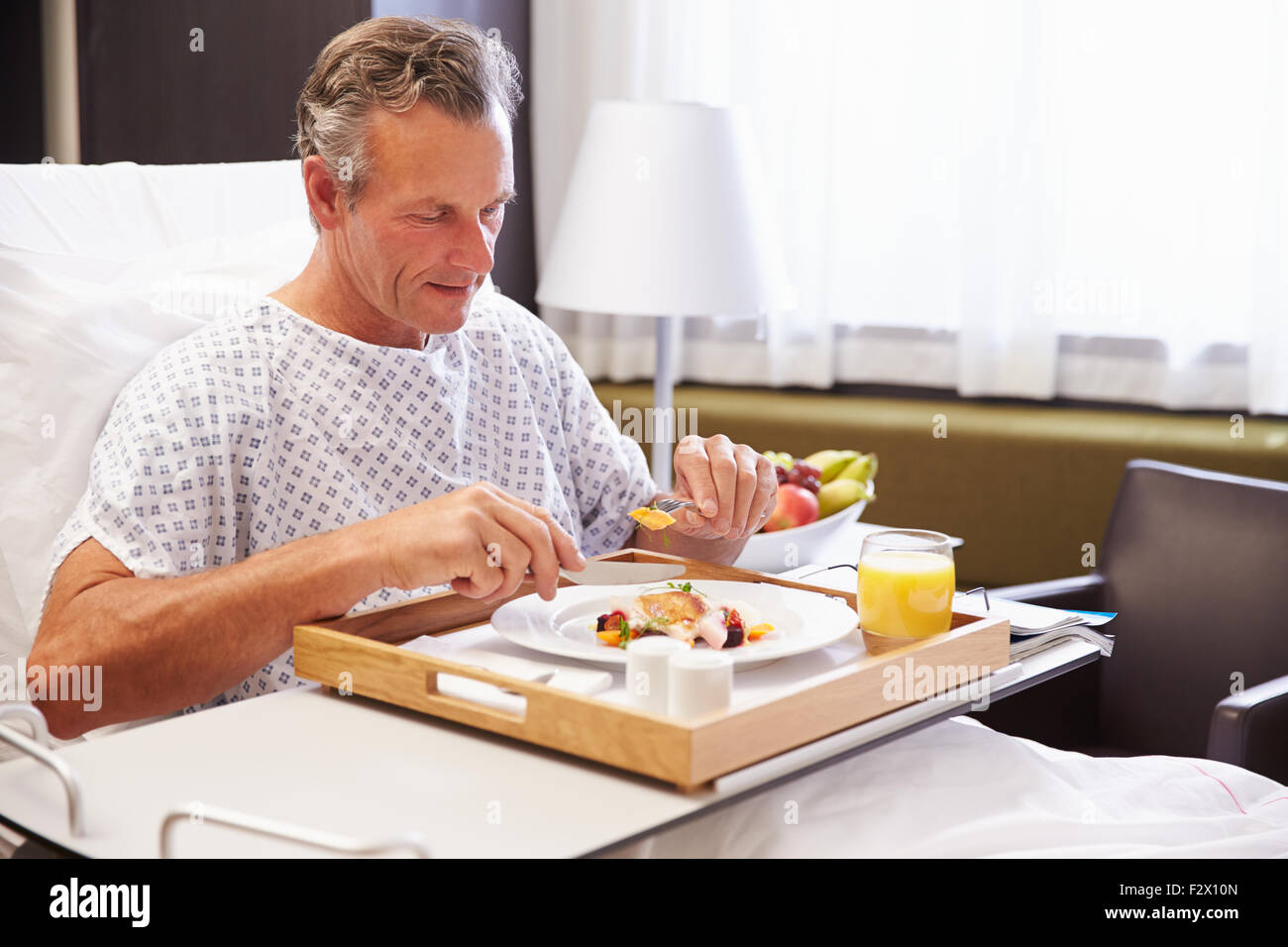 Paziente di sesso maschile nel letto di ospedale mangiare pasto dal vassoio Foto Stock