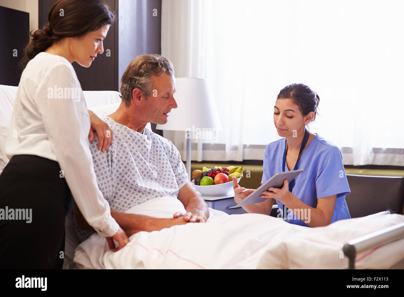 L'infermiera di parlare al paziente di sesso maschile e della moglie nel letto di ospedale Foto Stock