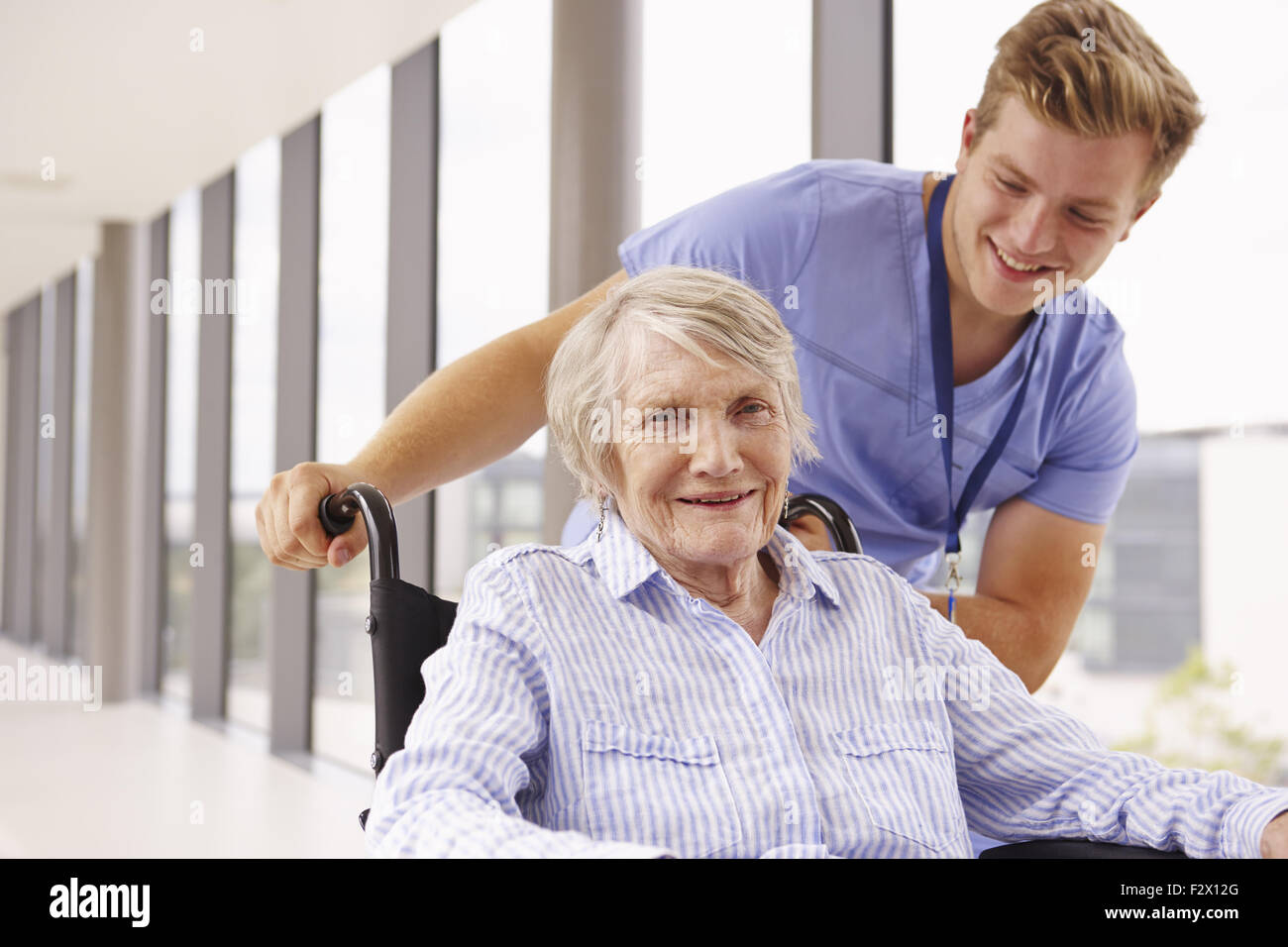 Infermiere spingendo Senior paziente in sedia a rotelle lungo il corridoio Foto Stock