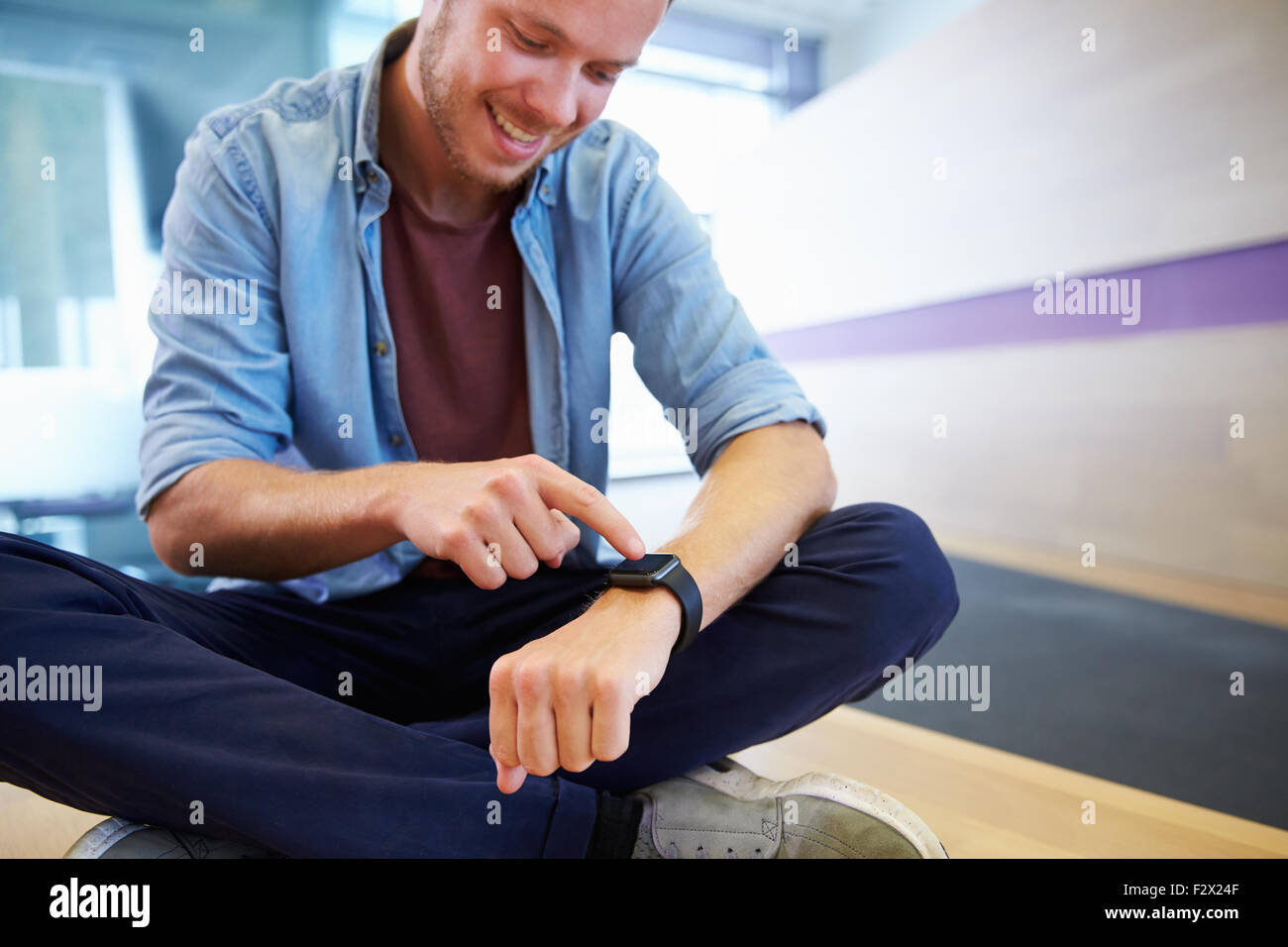 Casualmente vestito uomo si siede zampe trasversale rivolta verso il suo orologio Foto Stock