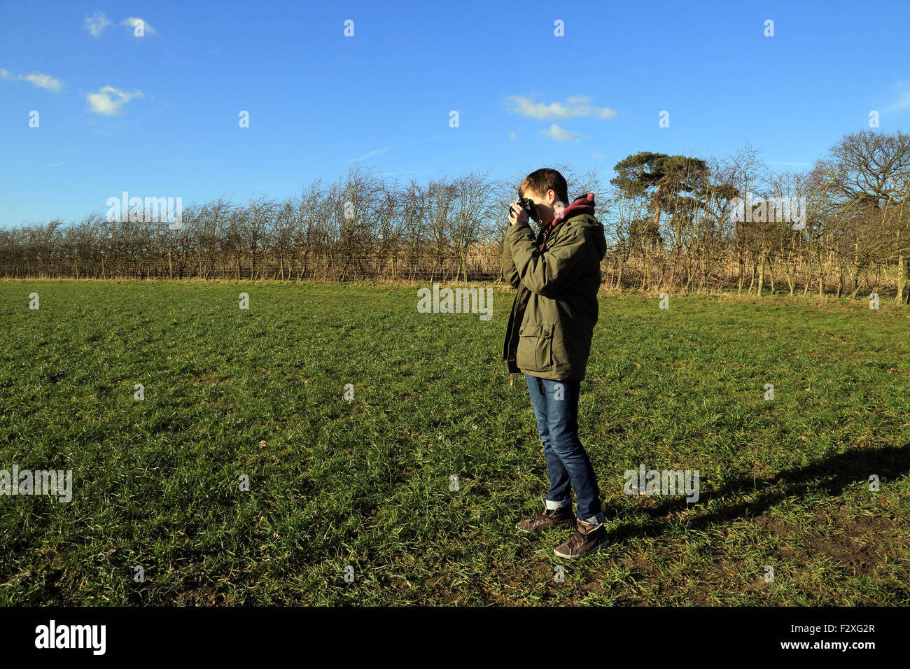 Ragazzo di 15 anni di prendere foto con pellicola 35mm Fotocamera nel campo in inverno a Brabourne fecce, Ashford, Kent, Inghilterra Foto Stock