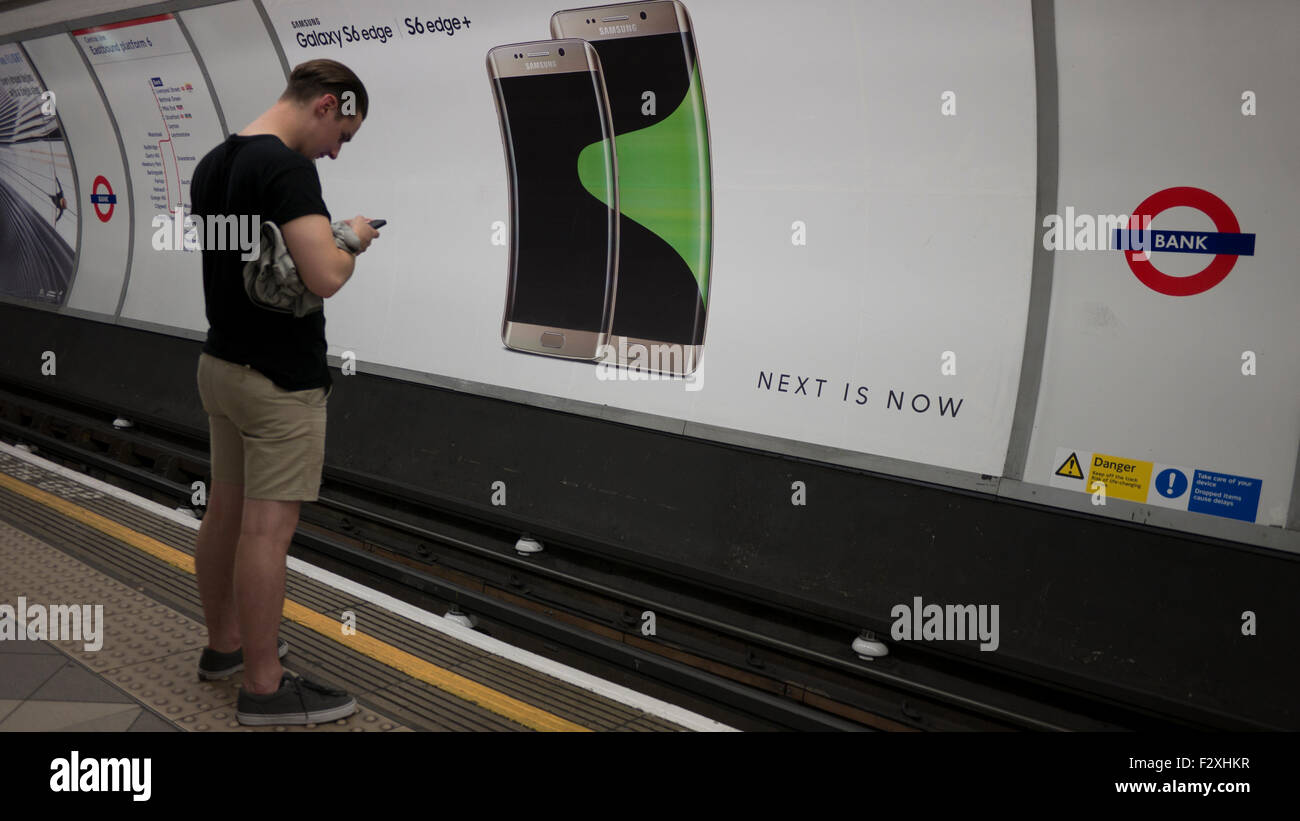 Maschio in cerca al telefono mobile nella parte anteriore del cartellone pubblicitario poster sulla metropolitana di Londra la visualizzazione di Samsung Galaxy S6 margine Foto Stock