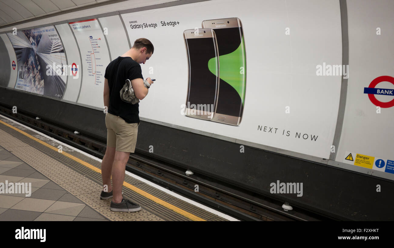 Maschio in cerca al telefono mobile nella parte anteriore del cartellone pubblicitario poster sulla metropolitana di Londra la visualizzazione di Samsung Galaxy S6 margine Foto Stock