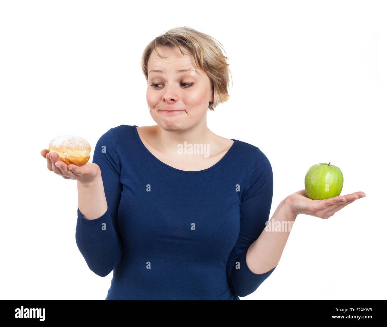 Giovane donna in possesso di una ciambella e un apple e ad essere più attratti da la ciambella, isolato su bianco Foto Stock