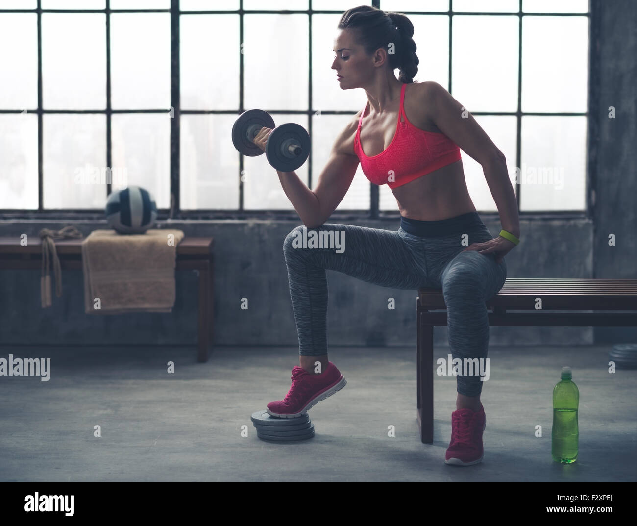 Sento che la masterizzazione! Un accoppiamento, sportivo giovane donna è seduta nel profilo su una panchina nel profilo, sollevamento pesi con una mano, mentre appoggia il suo gomito sul suo ginocchio. Foto Stock