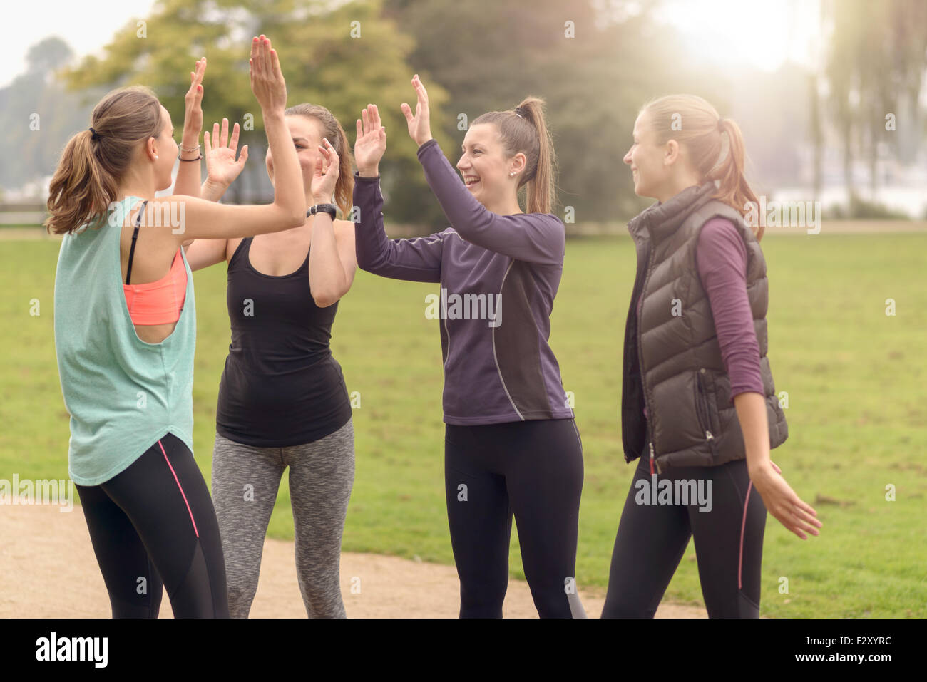 Quattro felici donne sane dando il doppio ad alta cinque gesto durante i momenti di relax dopo un esercizio all'aperto presso il parco. Foto Stock