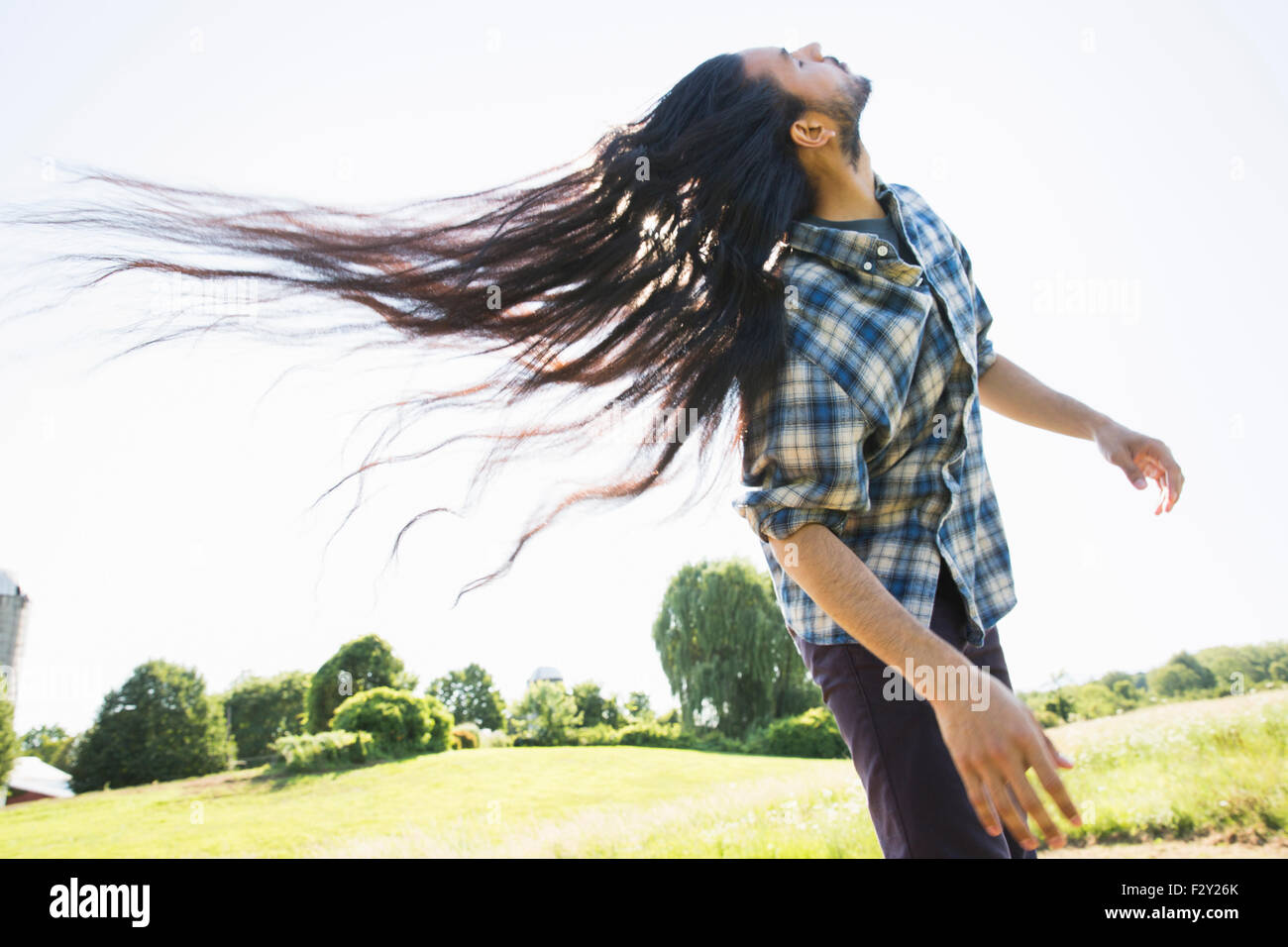 Un giovane uomo lasciando che la sua molto lunghi capelli scuri e scuotendo la testa per ventola all'aria fresca. Foto Stock