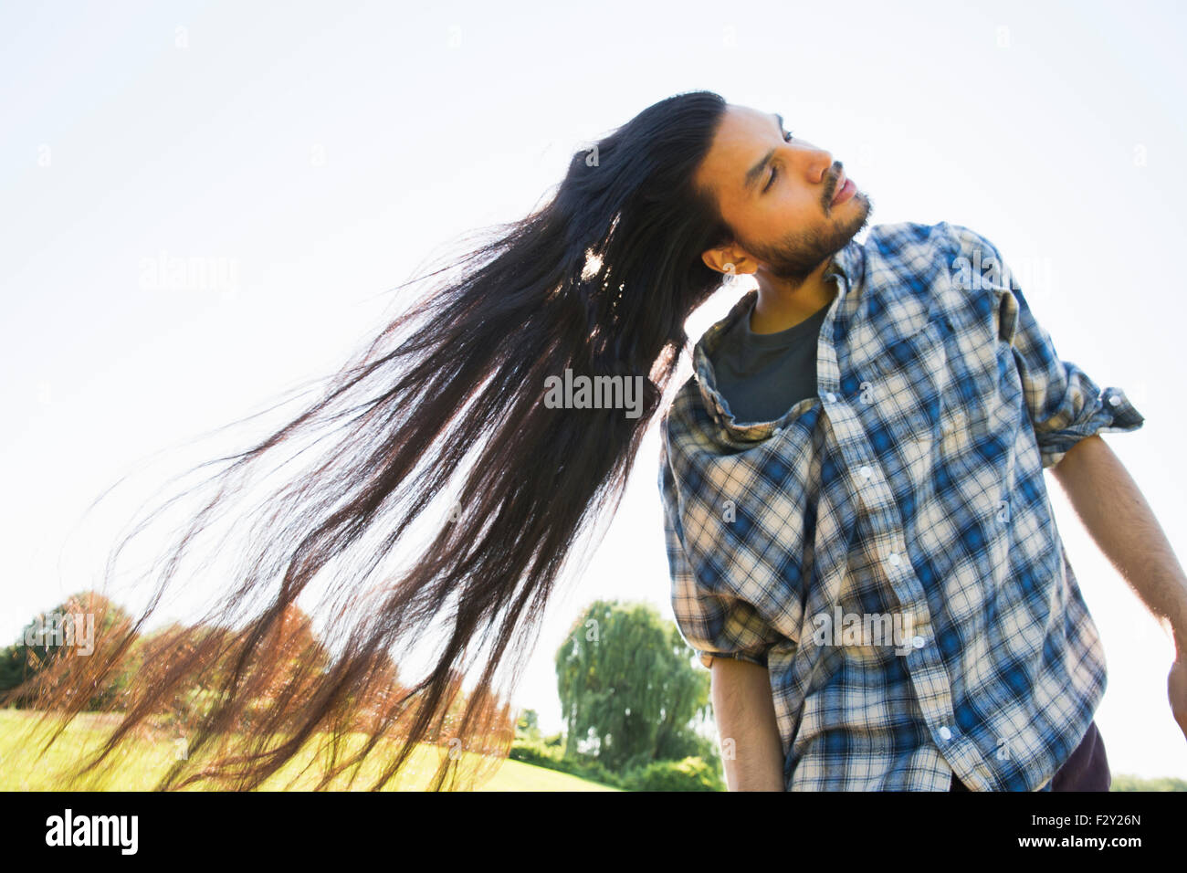 Un giovane uomo lasciando che la sua molto lunghi capelli scuri e scuotendo la testa per ventola all'aria fresca. Foto Stock