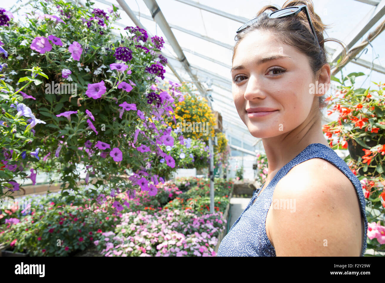 Una donna in piedi circondato da piante in fiore in una serra commerciale. Foto Stock