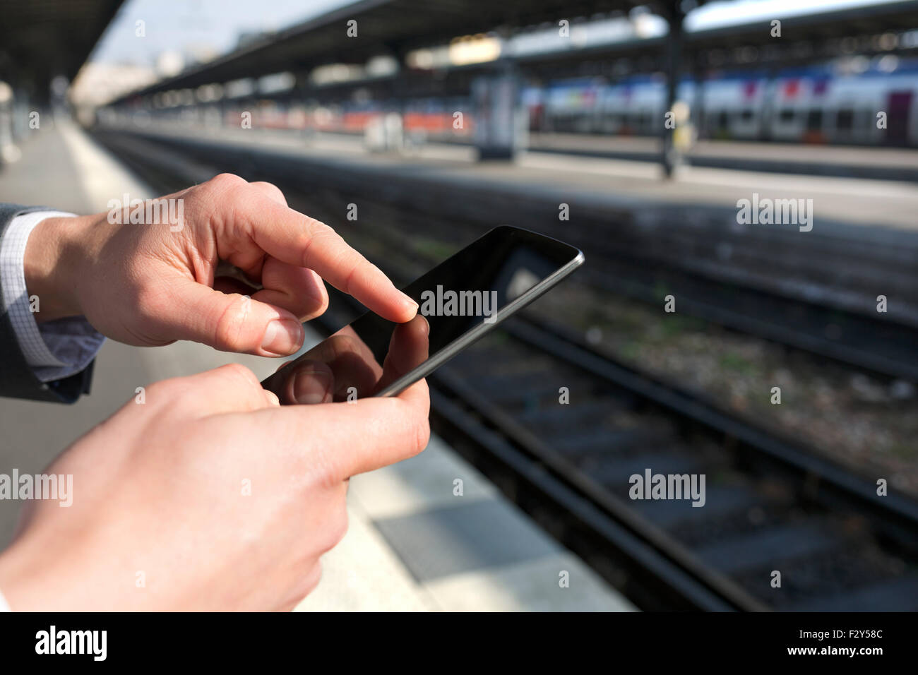 Uomo che utilizza un telefono cellulare sul vuoto piattaforma ferroviaria. Close-up le mani Foto Stock