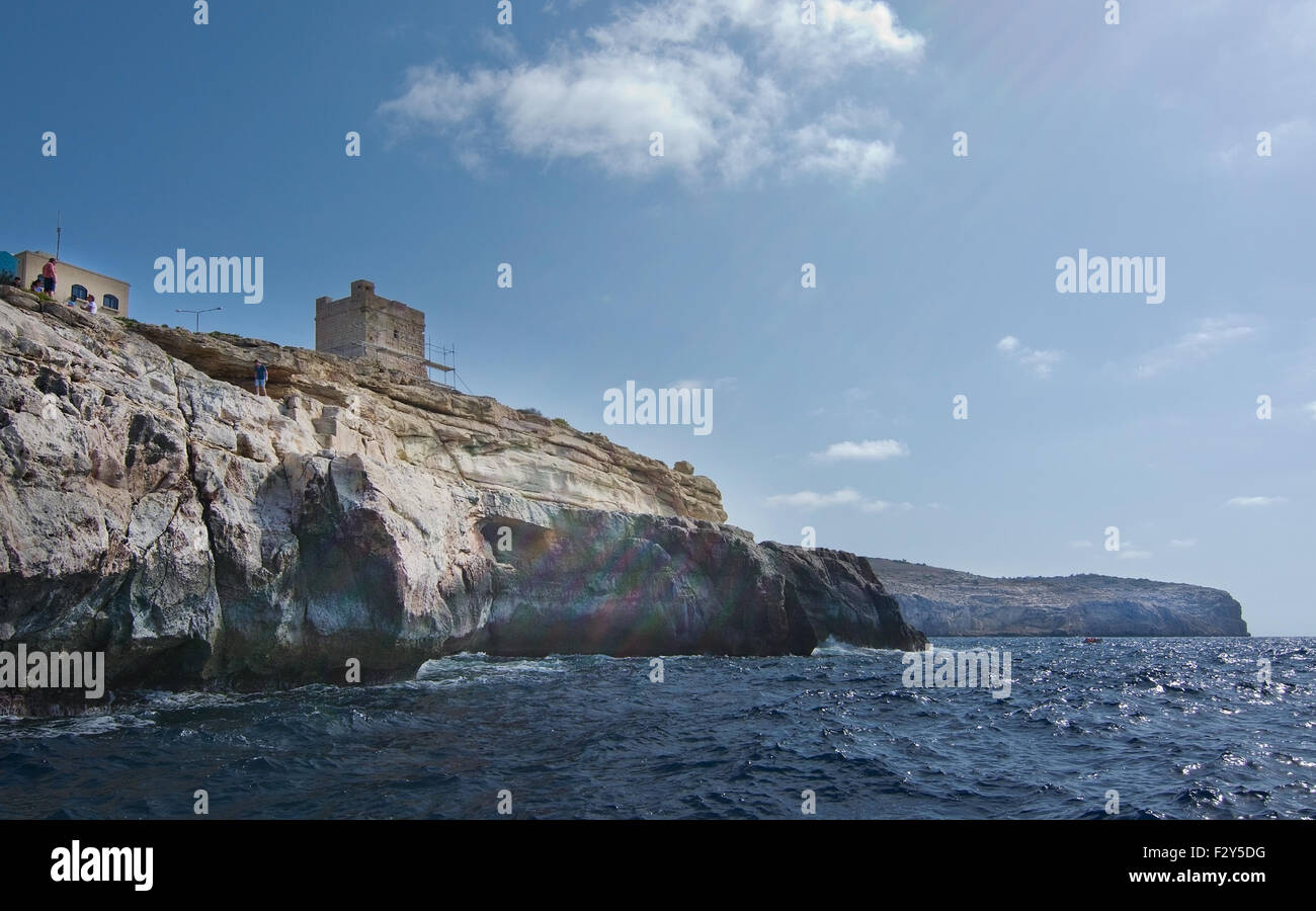 Rocce calcaree con grotte e limpide acque turchesi e la gente sulla cima della scogliera in Grotta Blu, Malta. Foto Stock