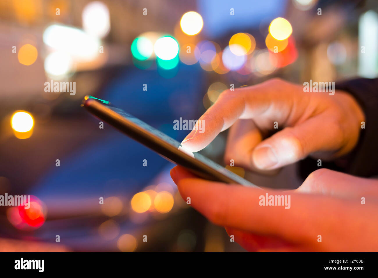 Uomo con il suo telefono cellulare in strada di notte di luce sullo sfondo bokeh di fondo Foto Stock