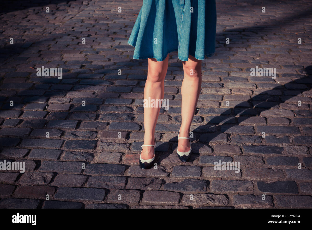 Una giovane donna che indossa un mantello e scarpe retrò sta camminando su una strada acciottolata al tramonto Foto Stock