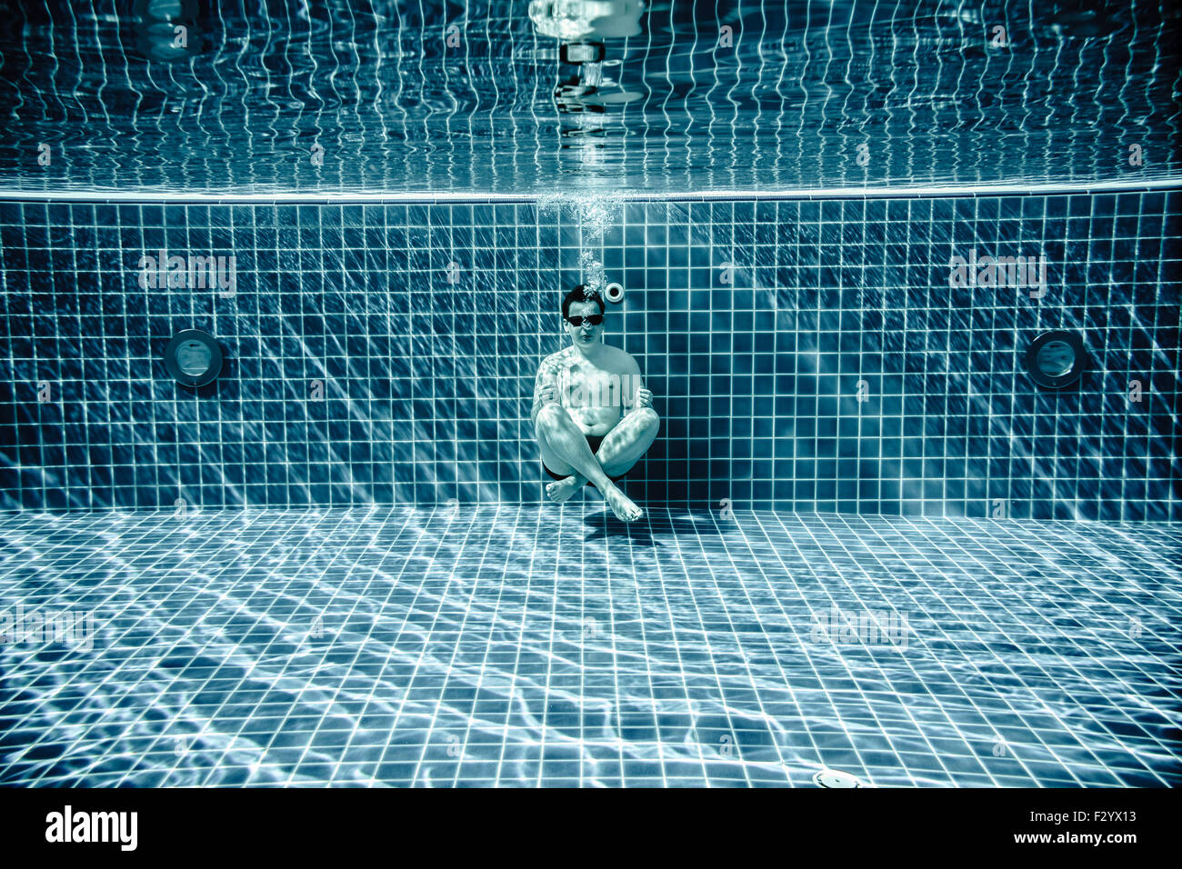 Uomo seduto sul fondo della piscina sotto l'acqua Foto Stock