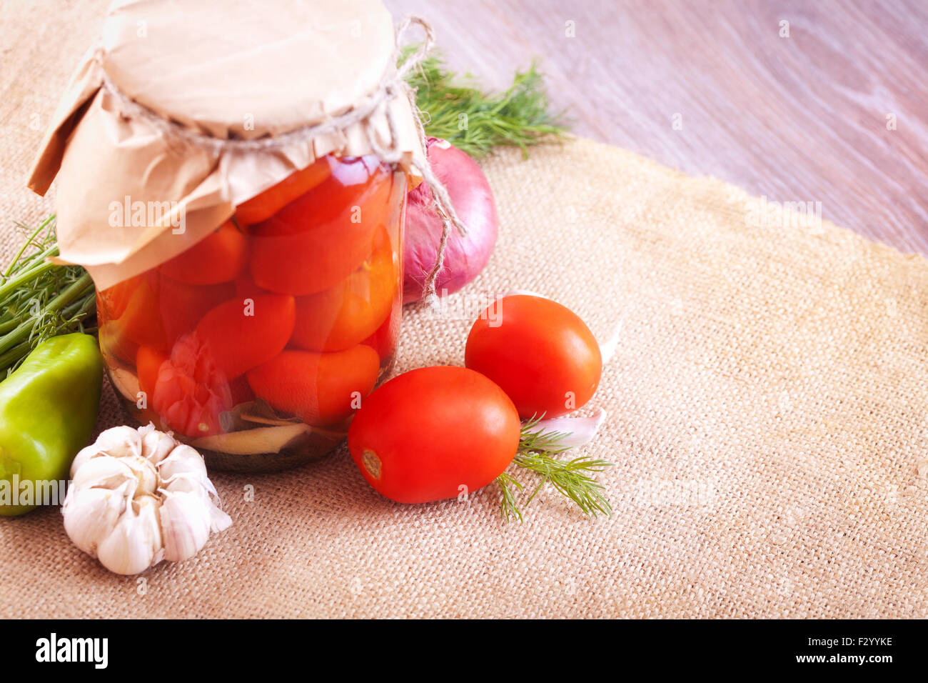 Pomodori marinati in vasetti con spezie e verdure su un tavolo di legno Foto Stock