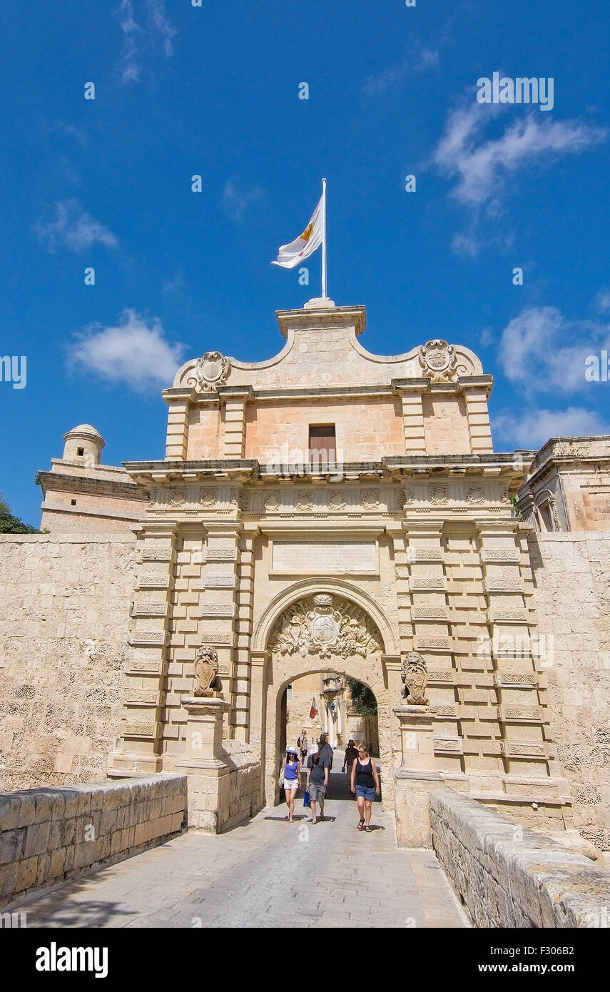 I turisti a piedi attraverso il barocco portale di ingresso con il flag per la città silenziosa in una giornata di sole nel mese di settembre in Mdina, Malta. Foto Stock