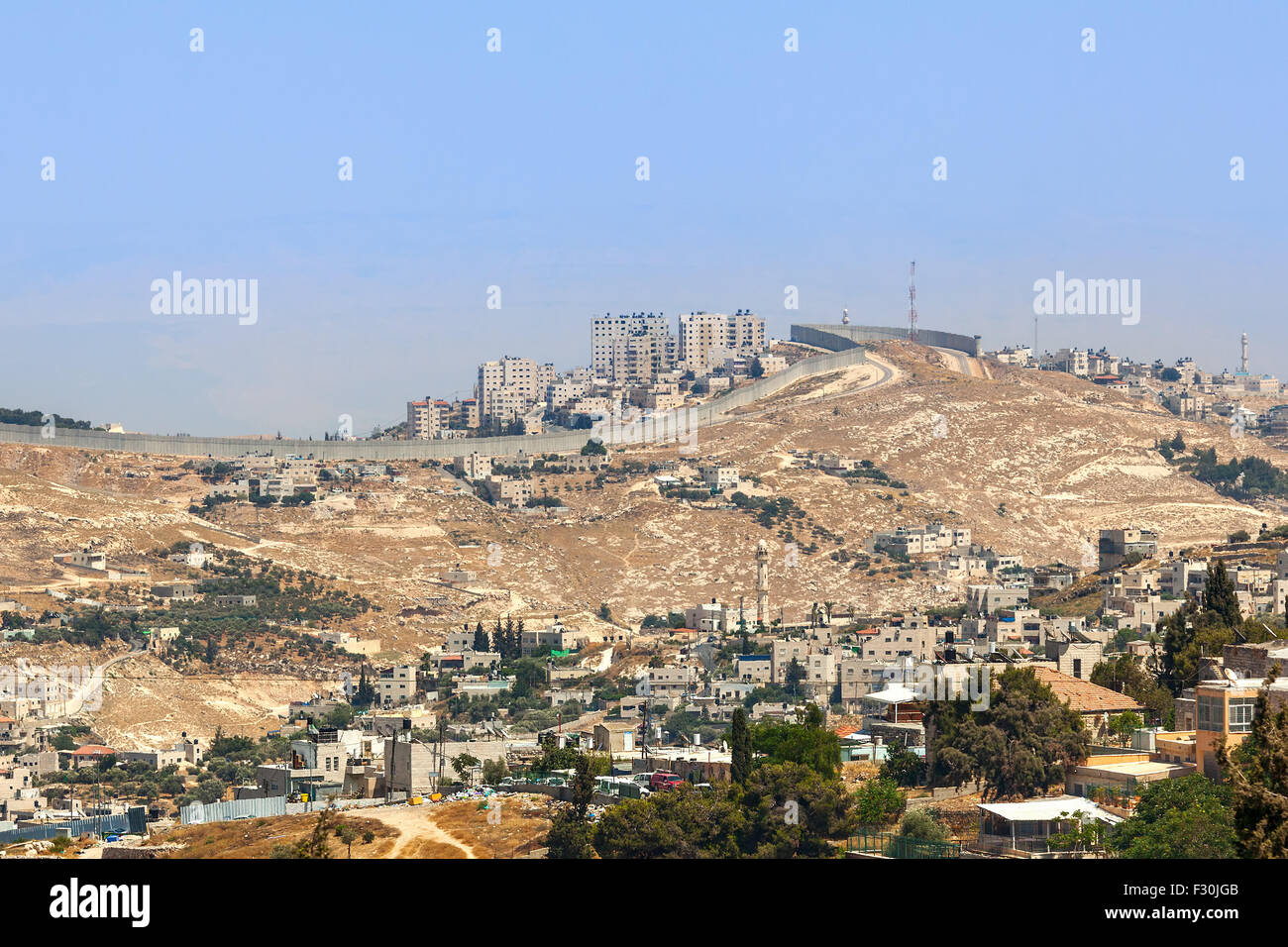 Villaggio palestinese e la città sulla collina dietro il muro di separazione in Cisgiordania in Israele. Foto Stock