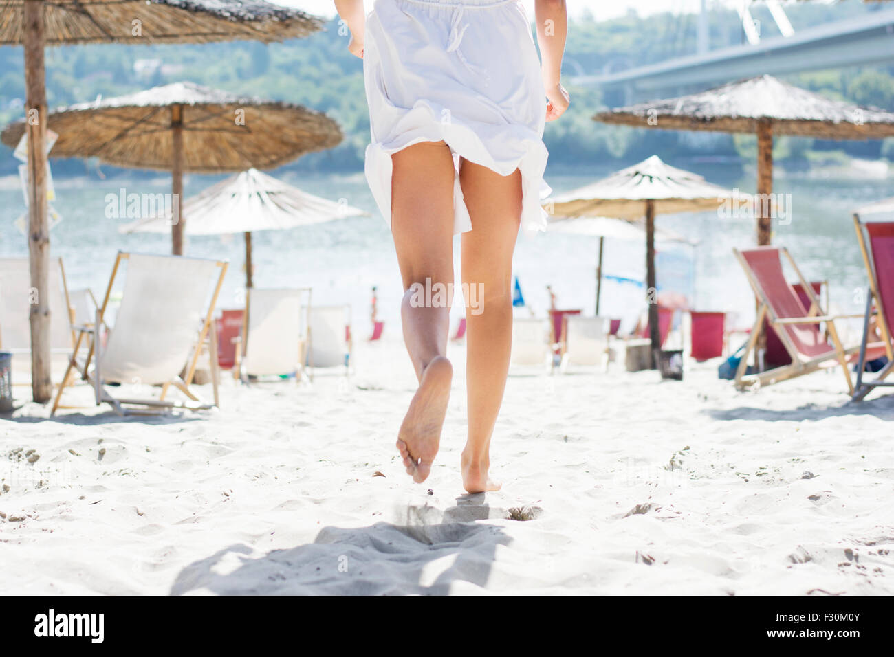 La donna in bianco abiti estivi in esecuzione sulla spiaggia di sabbia tra le sedie a sdraio e ombrelloni, in vista posteriore Foto Stock