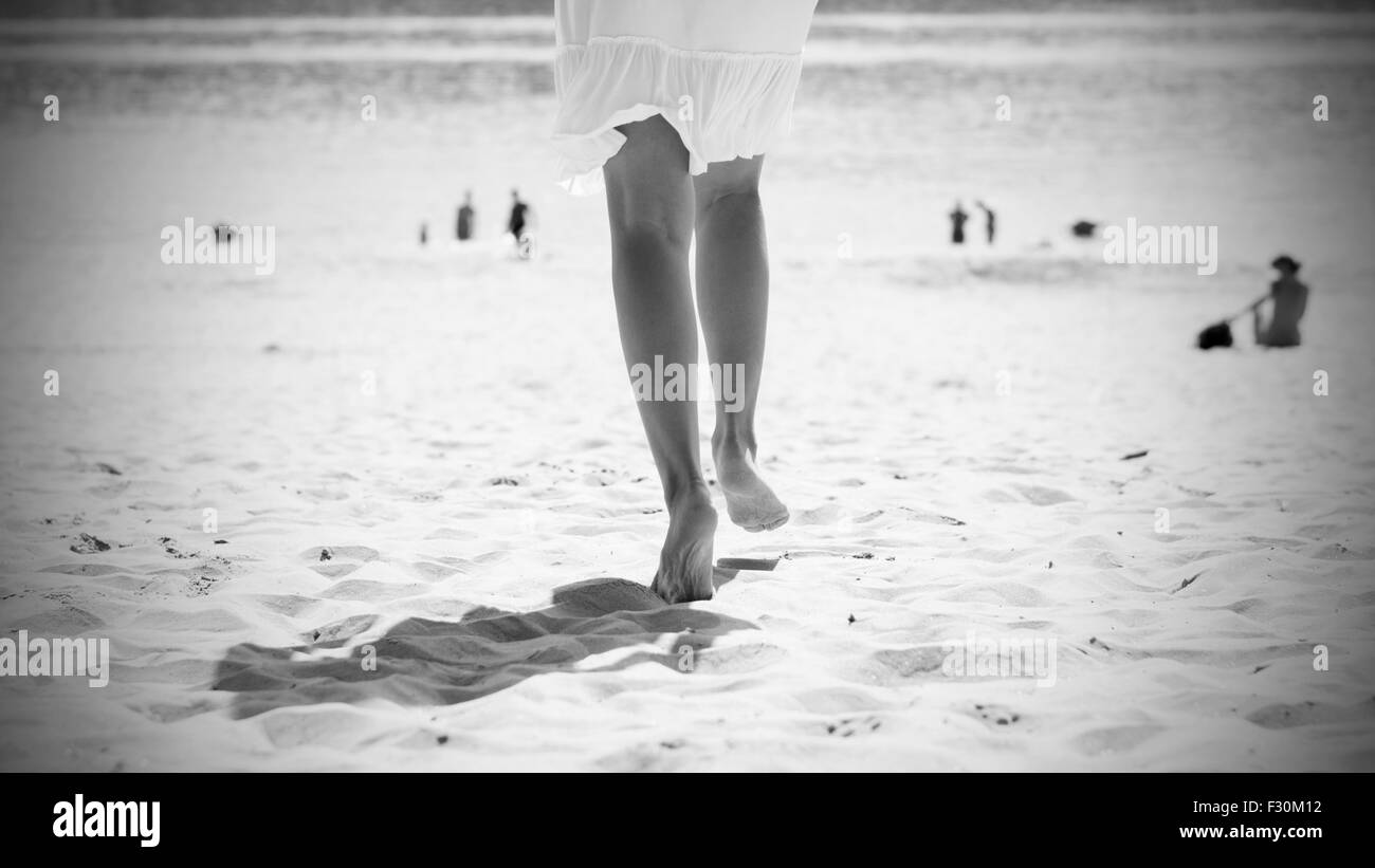 La donna in bianco abiti estivi in esecuzione sulla spiaggia sabbiosa di Costa del fiume ad estate burnout, vista posteriore e foto in bianco e nero. Foto Stock