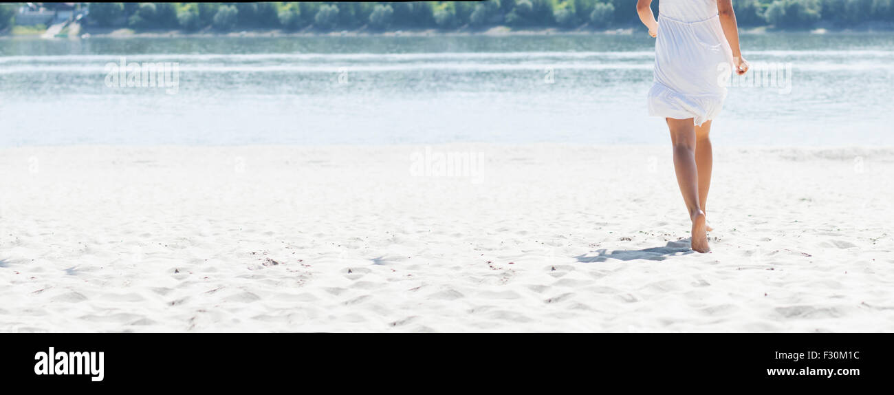 La donna in bianco abiti estivi in esecuzione sulla spiaggia sabbiosa di Costa del fiume ad estate burnout, vista posteriore, panorama foto. Foto Stock