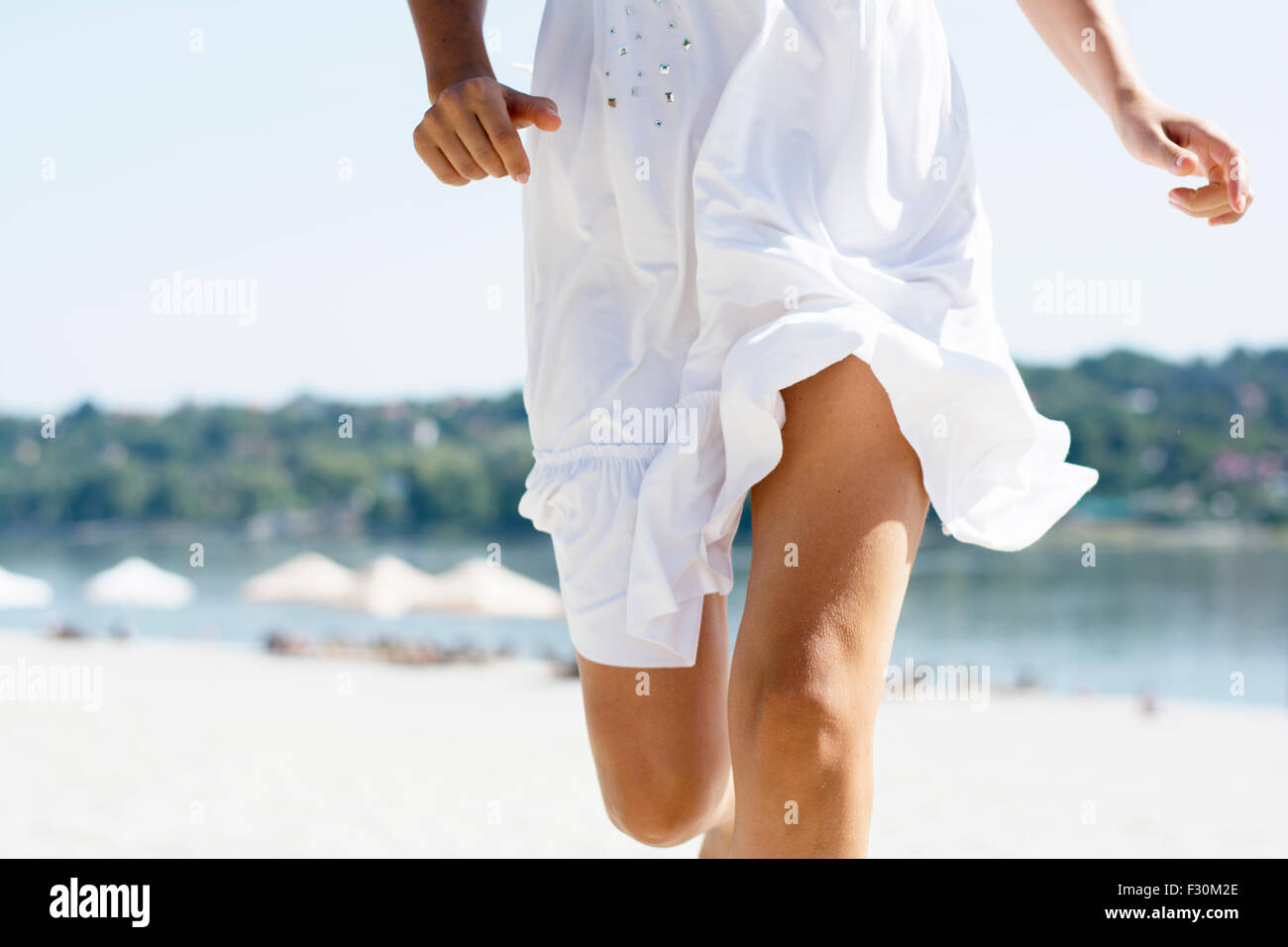 La donna in bianco abiti estivi in esecuzione sulla spiaggia sabbiosa di Costa del fiume ad estate burnout, vista frontale. Foto Stock