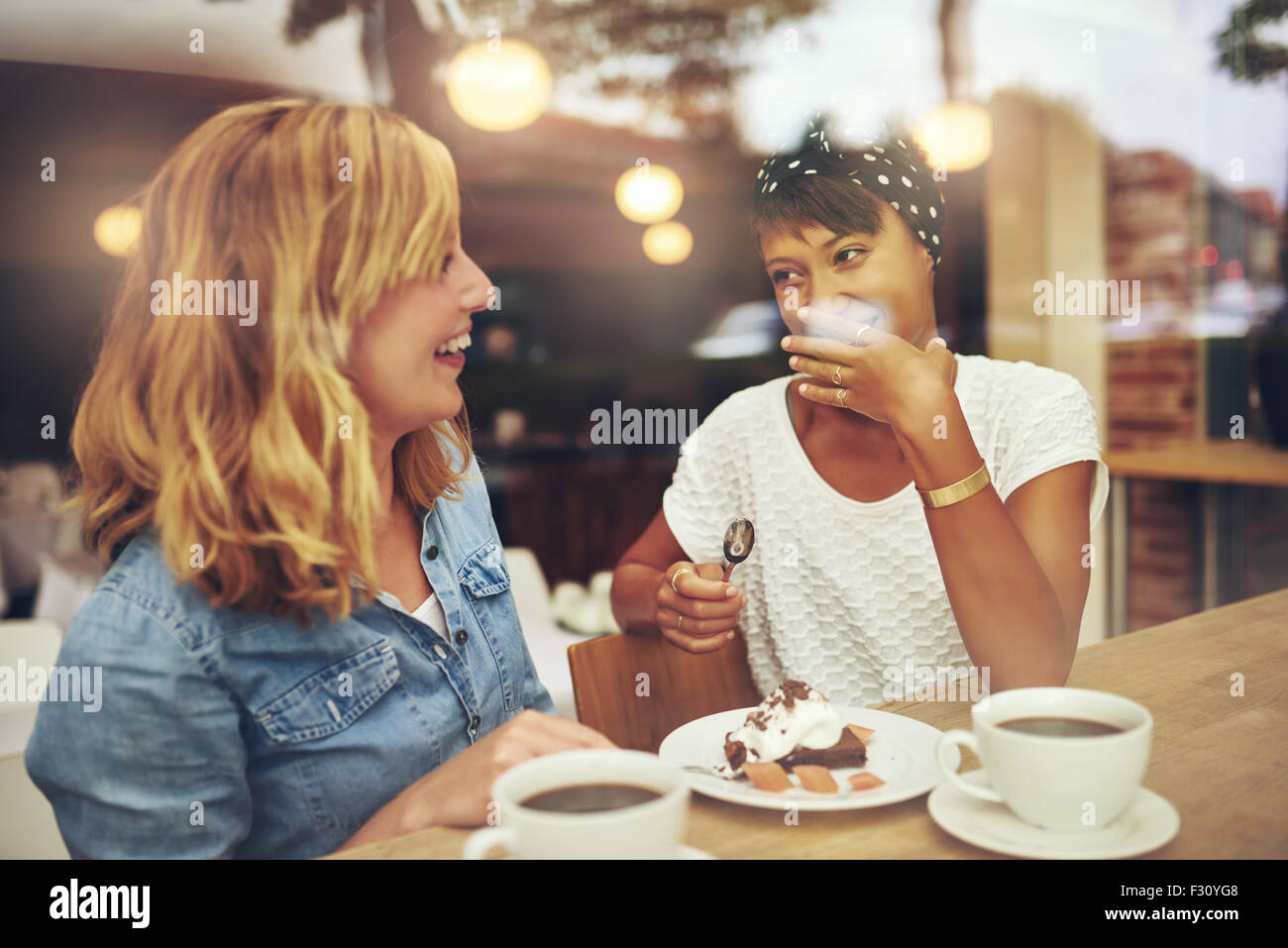 Due buone amiche gustando una tazza di caffè insieme in una caffetteria con una risata come le altre fa un gesto di em Foto Stock