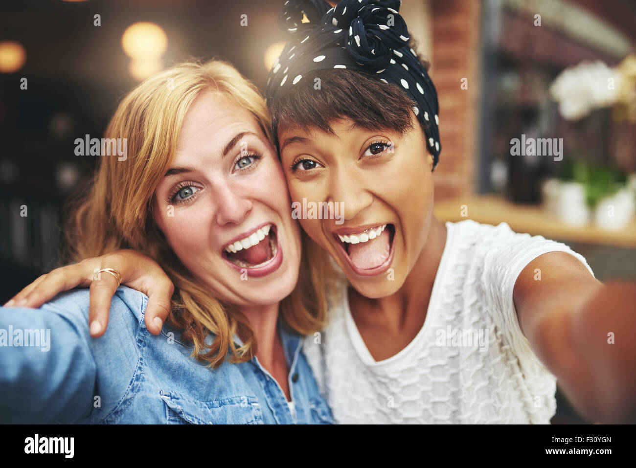 Esuberante felice multi etnico ragazza amici gustando un cordiale risata di fronte alla telecamera a braccetto all'interno di un coffee shop, testa Foto Stock