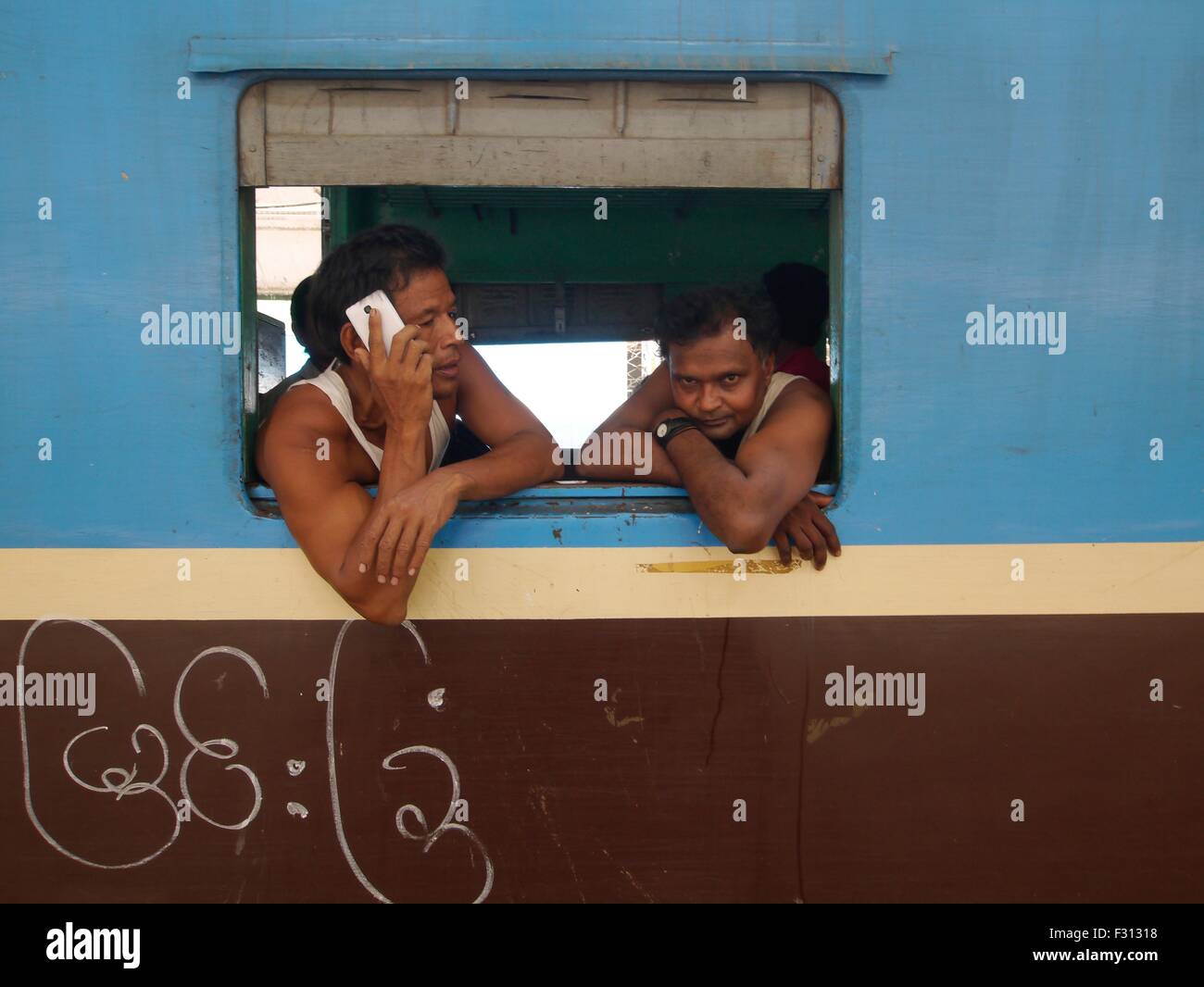 Un residente di Yangon sporgersi da una finestra del treno effettua una chiamata sul suo smartphone a Yangon, Myanmar. Con la recente apertura della sua economia al mondo, Myanmar ha visto un afflusso di moderna e conveniente di prodotti e servizi. Foto Stock