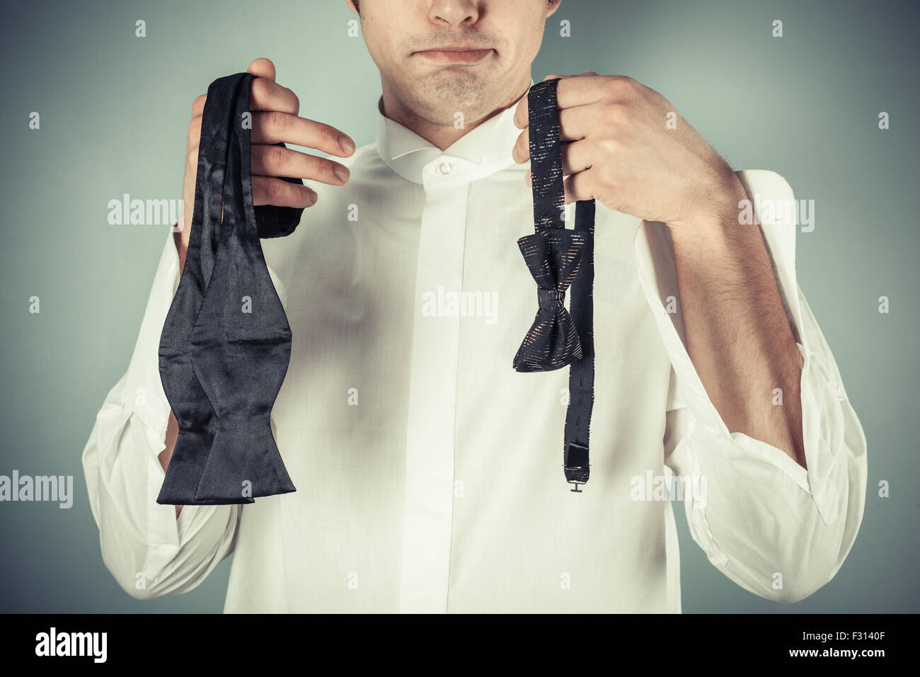 Giovane uomo di decidere se indossare una clip-on o a legare il suo proprio filtro bow tie Foto Stock
