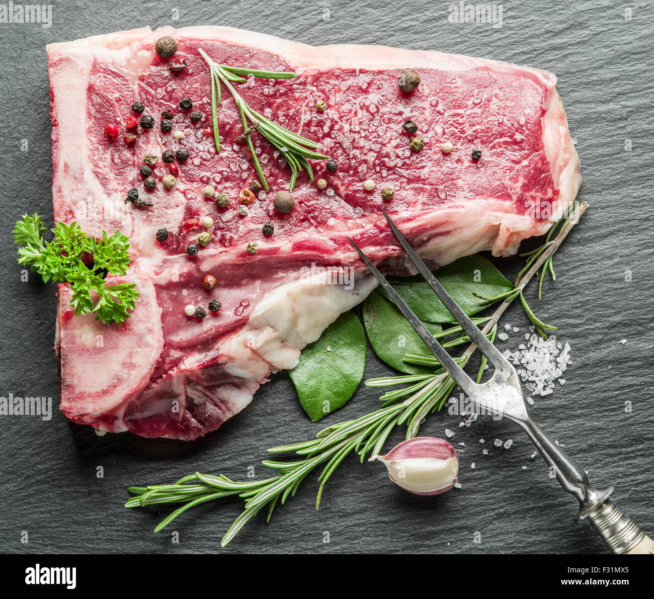 Raw bistecca di manzo con spezie sul nero tagliere. Foto Stock