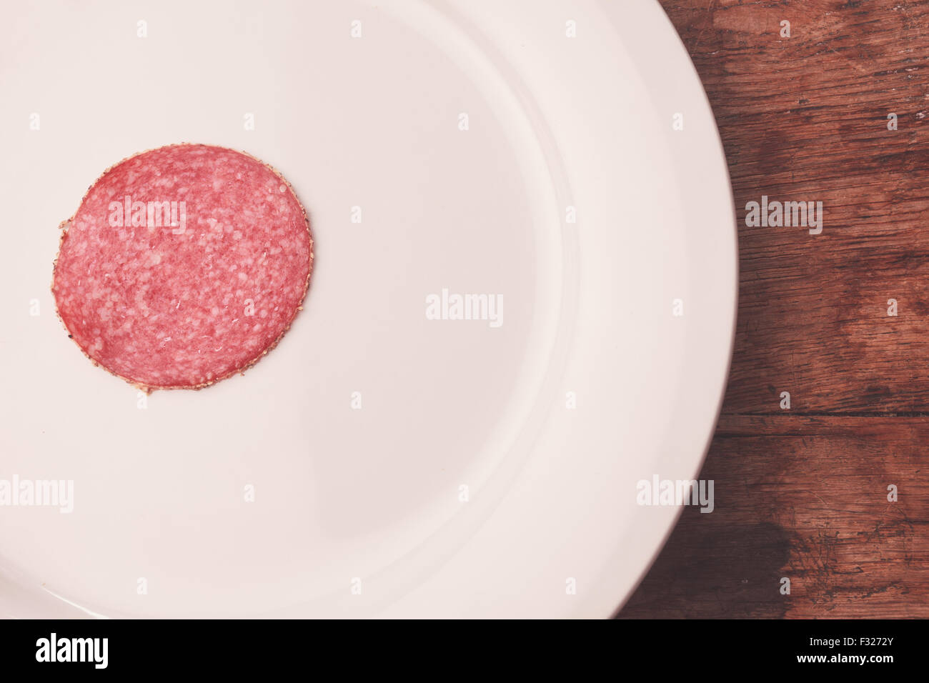 Un singolo pezzo di salame su una piastra bianca Foto Stock