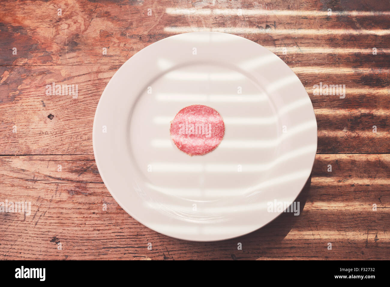 Un singolo pezzo di salame su una piastra bianca Foto Stock