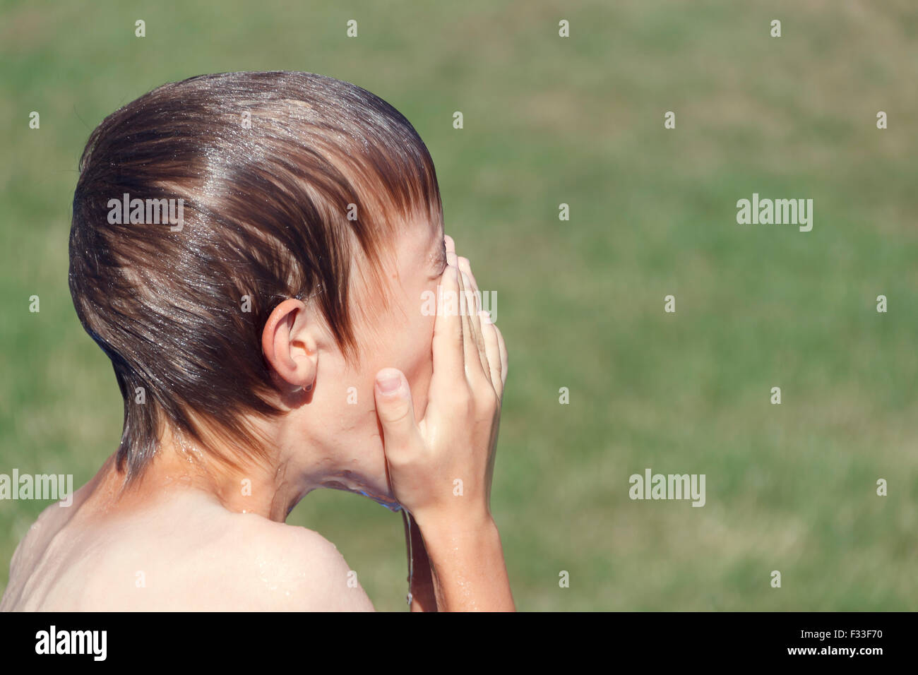 Ragazzo giovane all'aperto bagnato e strofinamento faccia. Foto Stock