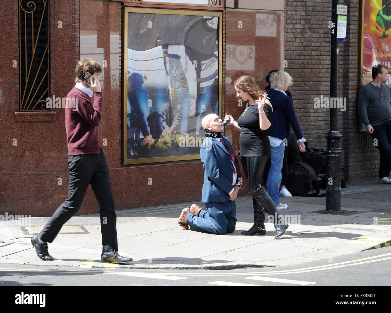 Un uomo umiliato pubblicamente da un dominatrix nelle strade di Soho, dove è stato realizzato a leccare il suo sputo e aveva sigarette stubbed fuori sulla sua linguetta come ha camminato intorno a carponi che indossa un collare doggy su una catena. Dotato di: Uomo pubblicamente hum Foto Stock