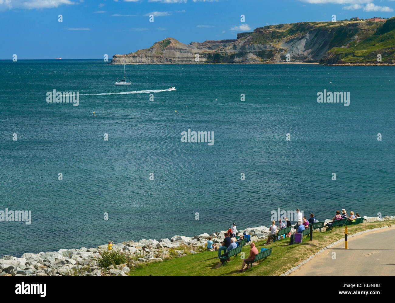 La gente seduta sulle panchine, ammirando il mare. in runswick bay, Inghilterra. Foto Stock