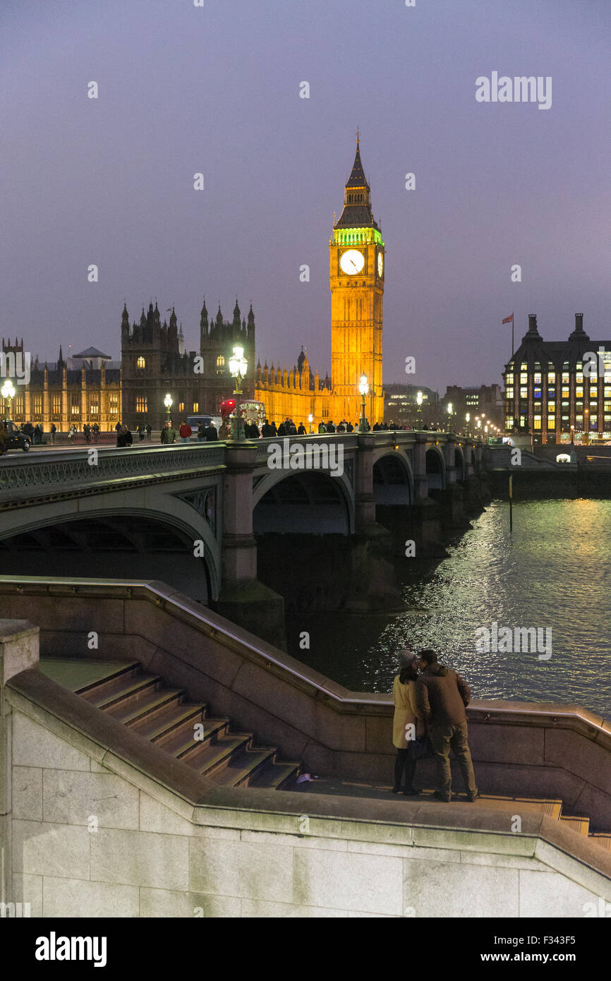 Un paio di baciare al tramonto sul terrapieno con il Big Ben e il palazzo di Westmintster e il fiume Tamigi oltre a Londra, Inghilterra Foto Stock