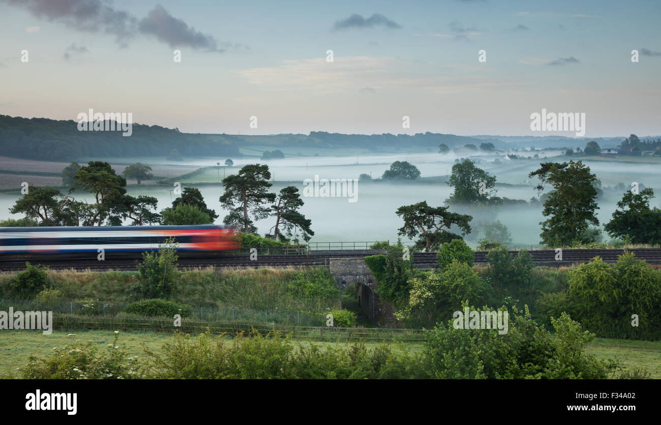 Il London Waterloo a Exeter treno passa Milborne stoppino in una nebbiosa mattina d'estate, Somerset, Inghilterra, Regno Unito Foto Stock