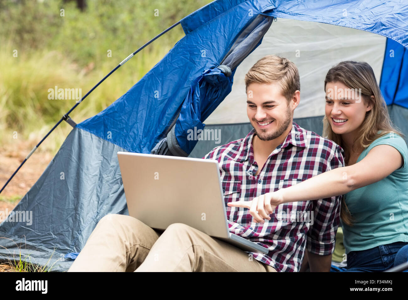 Giovani piuttosto escursionista giovane seduto in una tenda guardando al laptop Foto Stock
